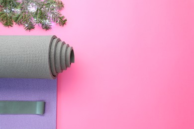 Photo of Yoga mat, elastic band, Christmas lights and fir branches on pink background, flat lay. Space for text