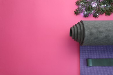 Photo of Yoga mat, elastic band, Christmas lights and fir branches on pink background, flat lay. Space for text