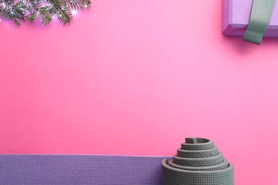 Photo of Yoga mat, elastic band, Christmas lights and fir branches on pink background, flat lay. Space for text