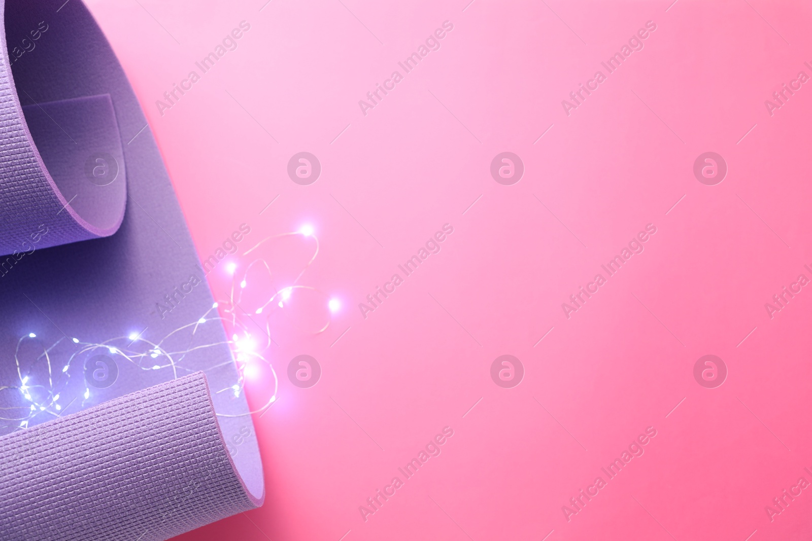 Photo of Yoga mat and Christmas lights on pink background, top view. Space for text