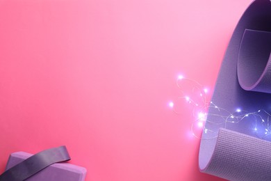 Photo of Yoga mat, block, elastic band and Christmas lights on pink background, flat lay. Space for text