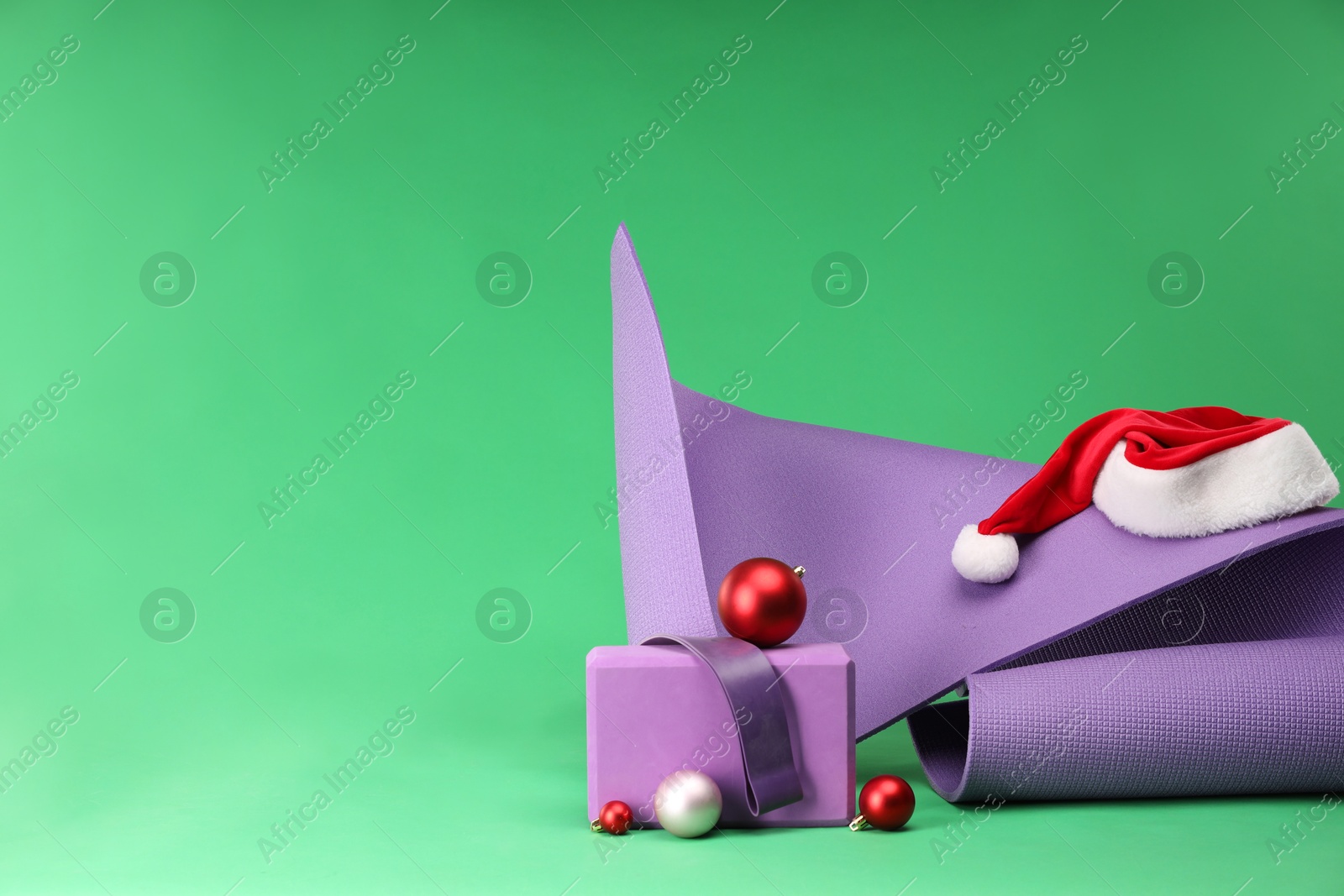 Photo of Yoga mat, block, Santa hat and baubles on green background, space for text