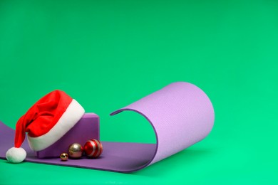 Photo of Yoga mat, block, Santa hat and baubles on green background