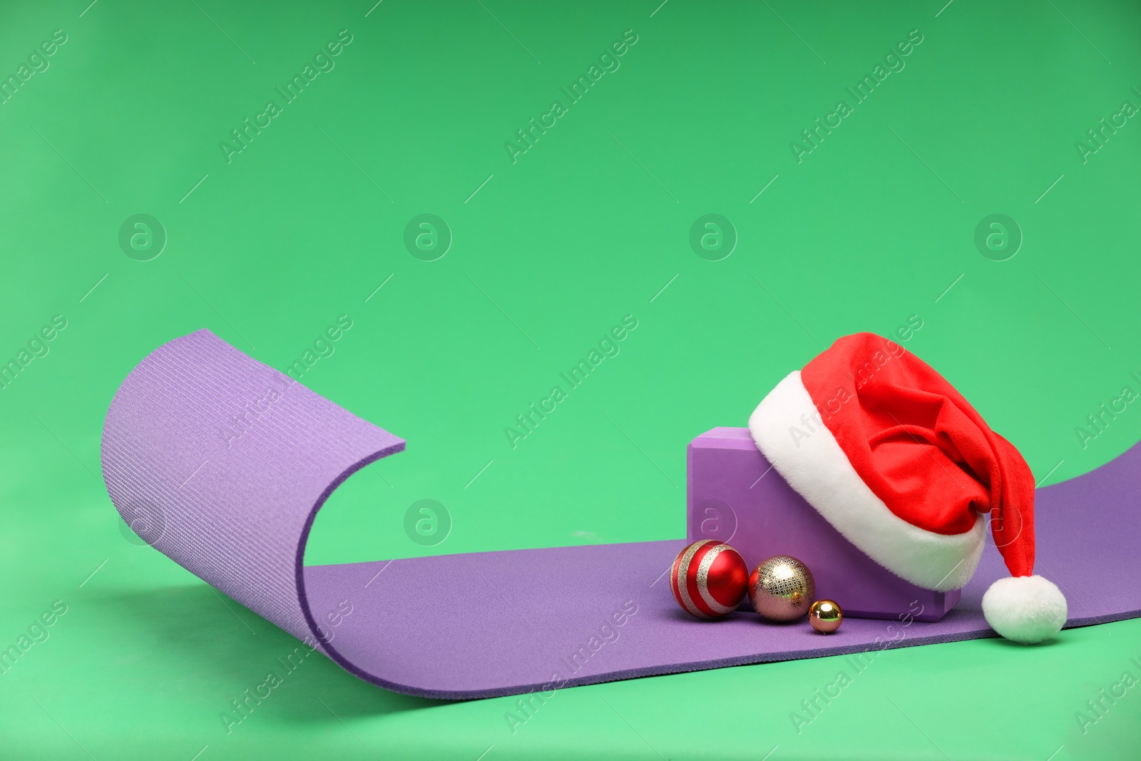 Photo of Yoga mat, block, Santa hat and baubles on green background