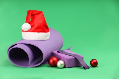 Photo of Yoga mat, block, Santa hat and baubles on green background. Space for text