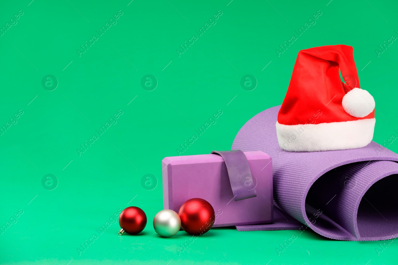 Photo of Yoga mat, block, Santa hat and baubles on green background, space for text