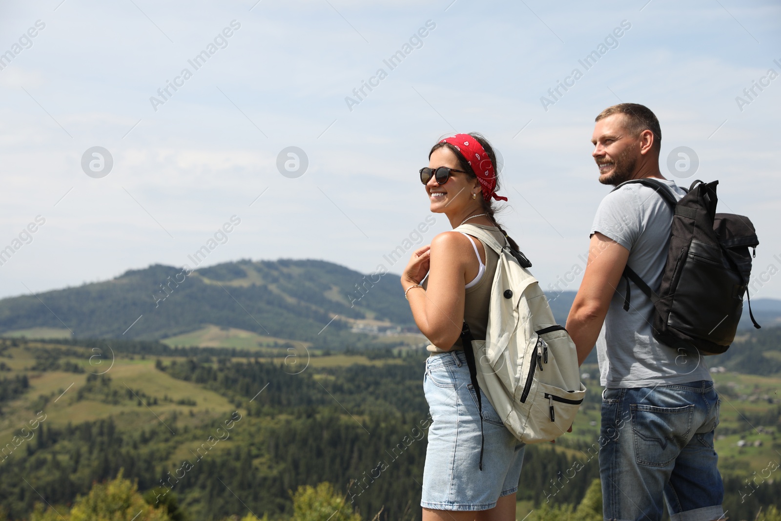 Photo of Happy couple with backpacks enjoying picturesque landscape, space for text. Active tourism