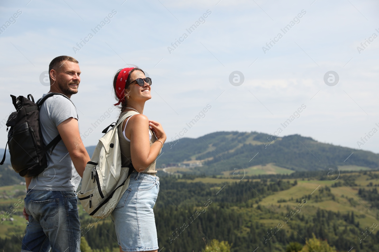 Photo of Happy couple with backpacks enjoying picturesque landscape, space for text. Active tourism