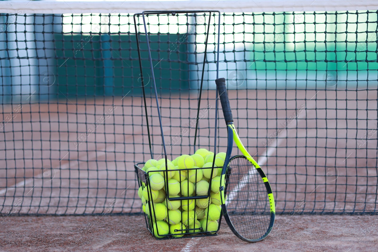 Photo of Tennis racket and balls in metal basket on court