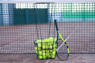 Tennis racket and balls in metal basket on court