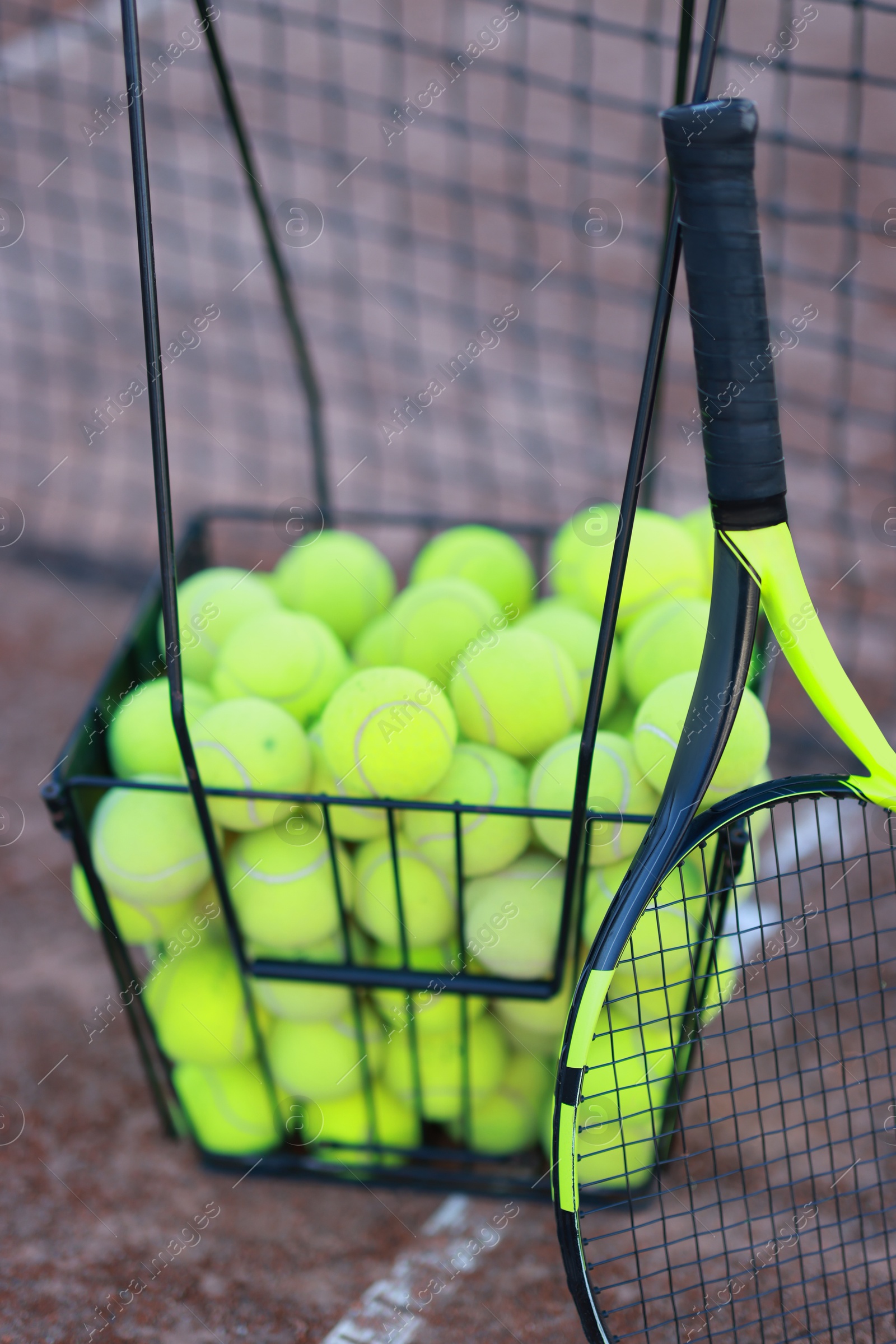 Photo of Tennis racket and balls in metal basket on court