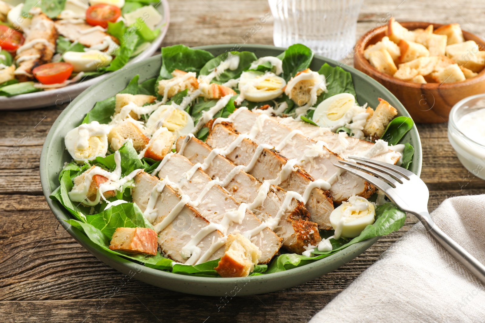 Photo of Delicious Caesar salad with chicken on wooden table, closeup