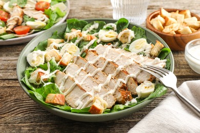 Delicious Caesar salad with chicken on wooden table, closeup