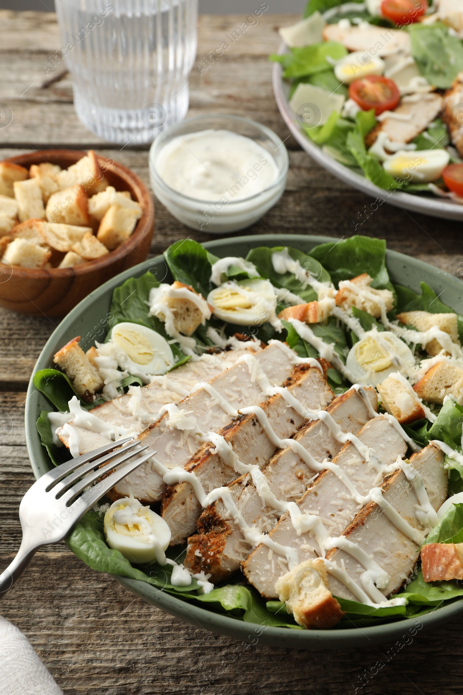 Photo of Delicious Caesar salad with chicken on wooden table, closeup