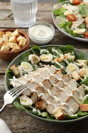 Photo of Delicious Caesar salad with chicken on wooden table, closeup