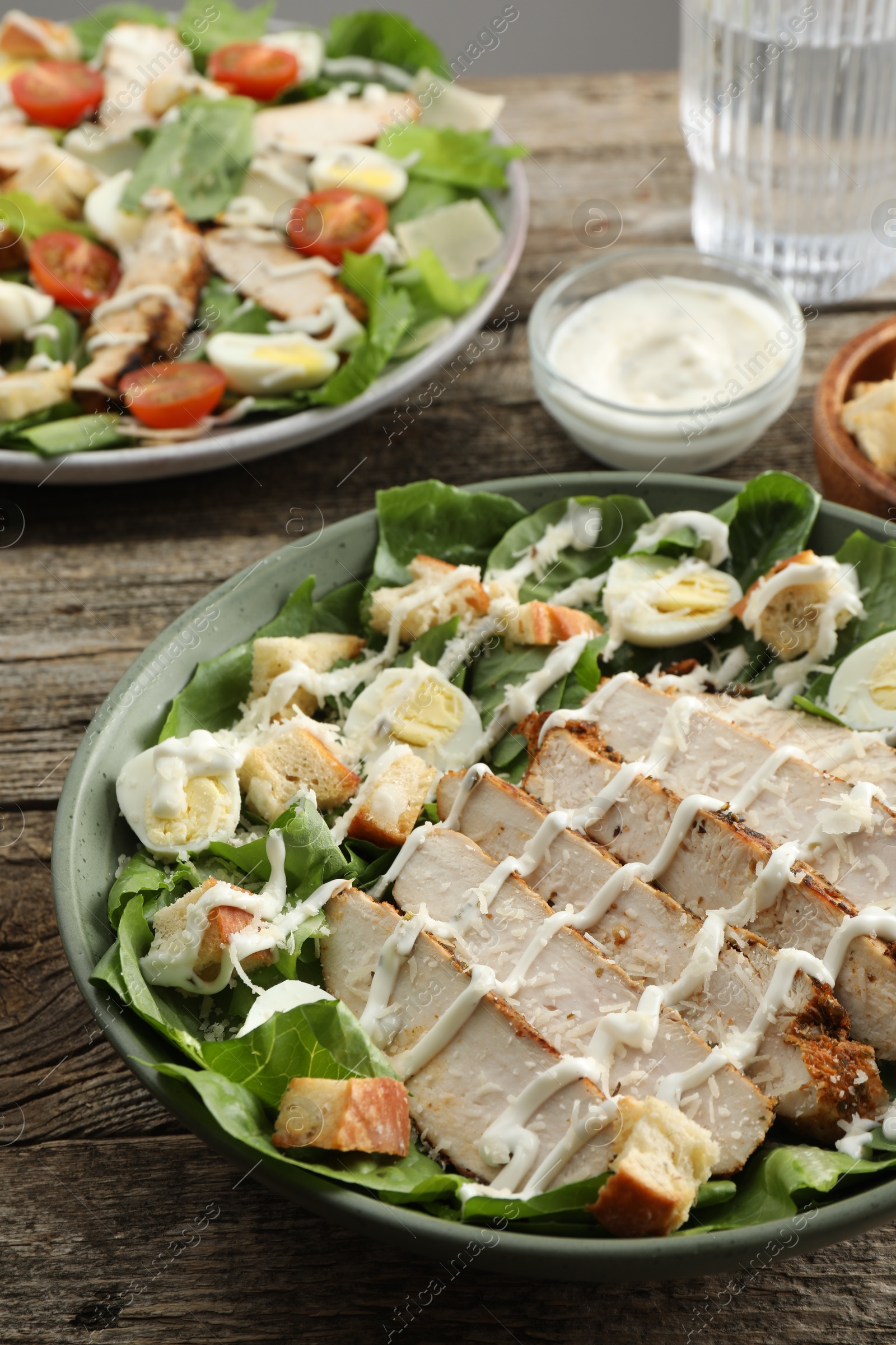 Photo of Delicious Caesar salad with chicken on wooden table, closeup