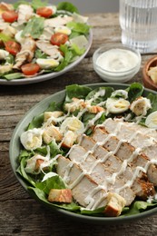 Photo of Delicious Caesar salad with chicken on wooden table, closeup