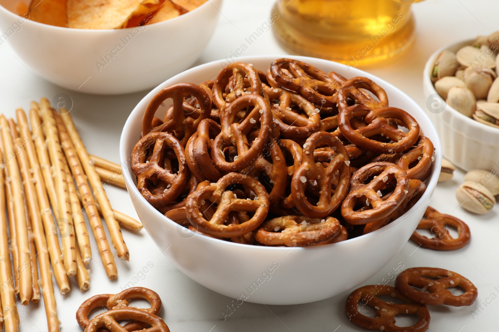 Photo of Delicious pretzel crackers and other snacks on white table, closeup