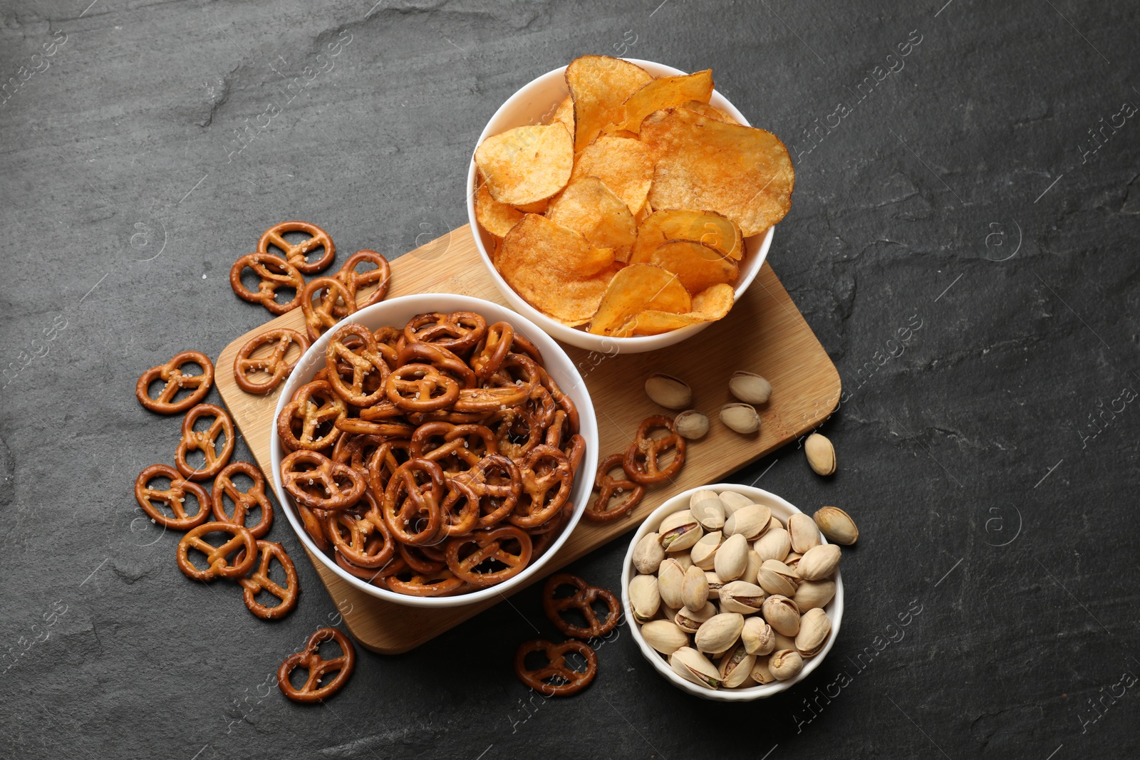 Photo of Delicious pretzel crackers and other snacks on black table, flat lay