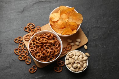 Photo of Delicious pretzel crackers and other snacks on black table, flat lay