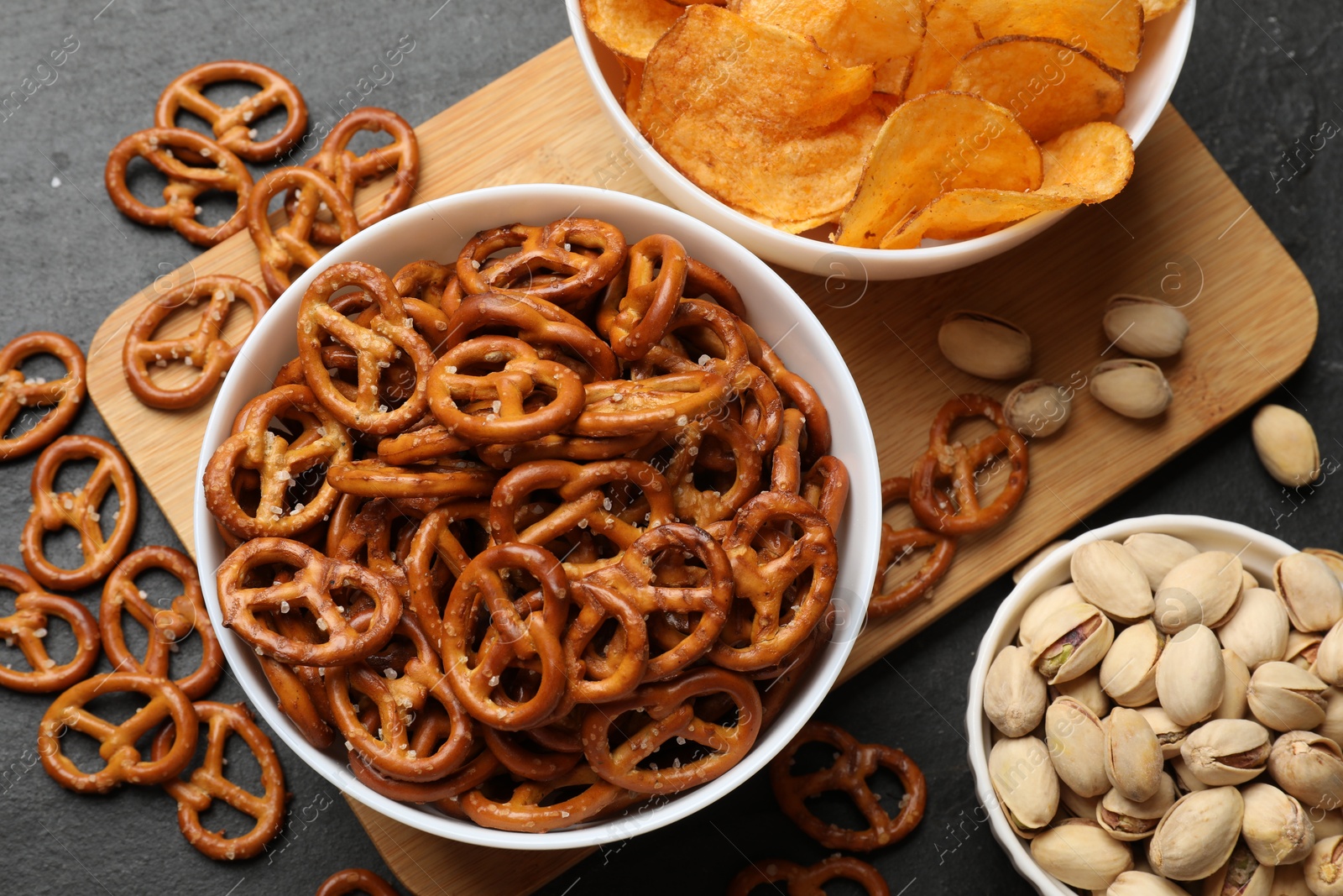 Photo of Delicious pretzel crackers and other snacks on black table, flat lay