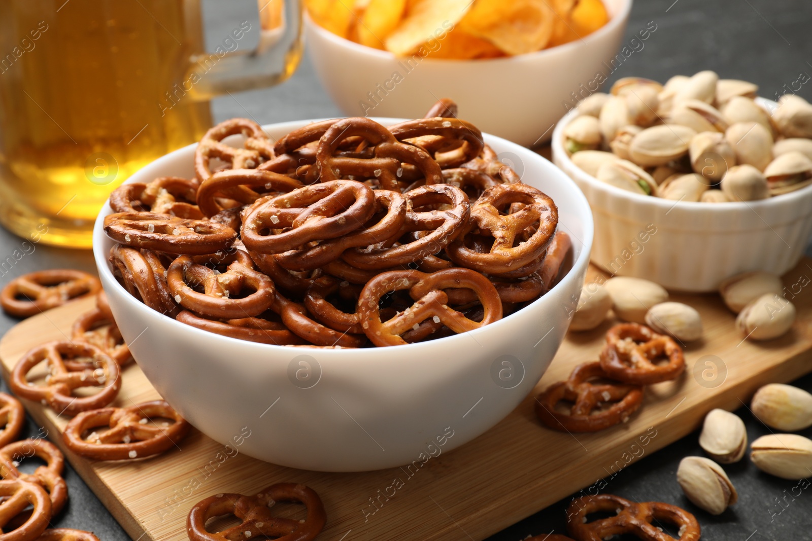 Photo of Delicious pretzel crackers, beer and other snacks on black table, closeup