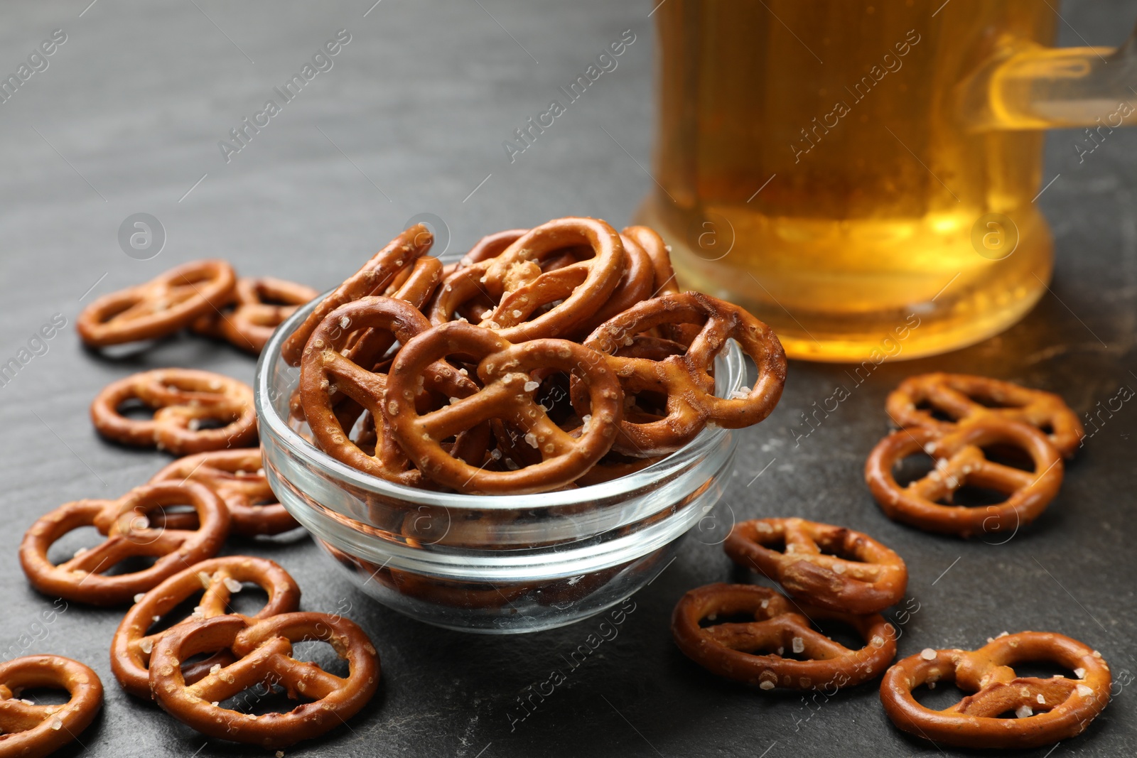 Photo of Delicious salty pretzel crackers and beer on black table, closeup