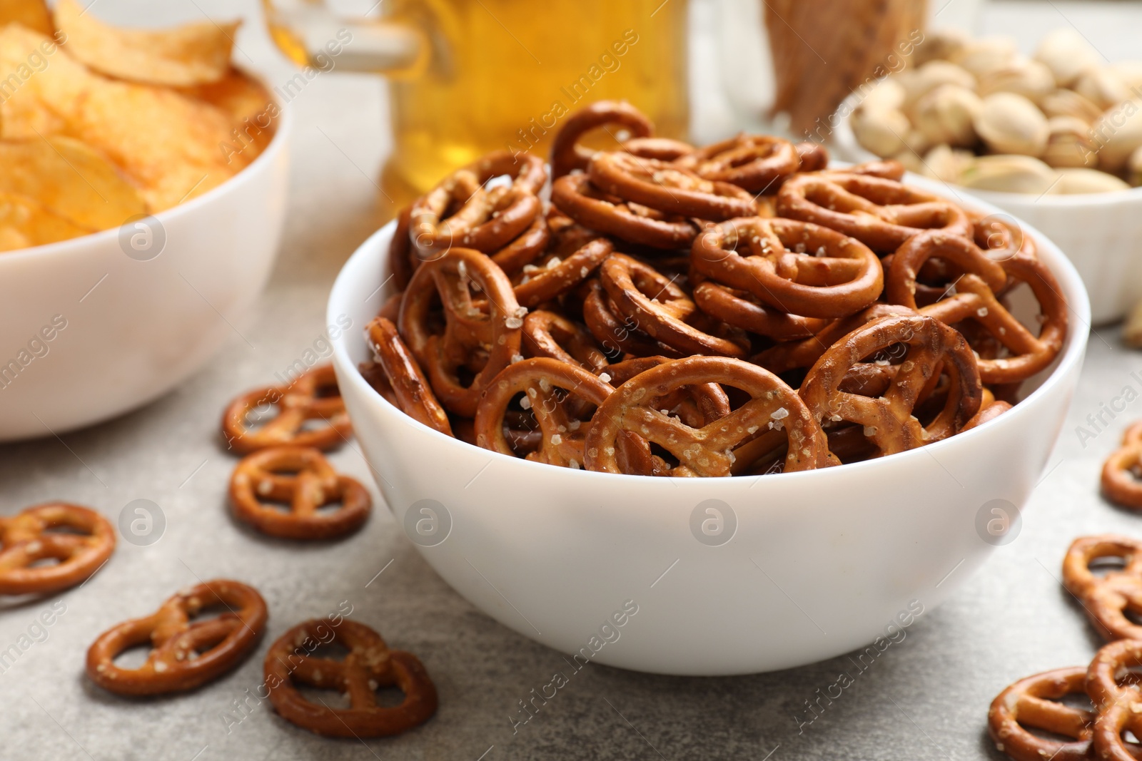 Photo of Delicious pretzel crackers, beer and other snacks on light table, closeup