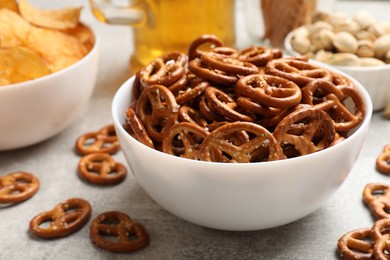 Photo of Delicious pretzel crackers, beer and other snacks on light table, closeup