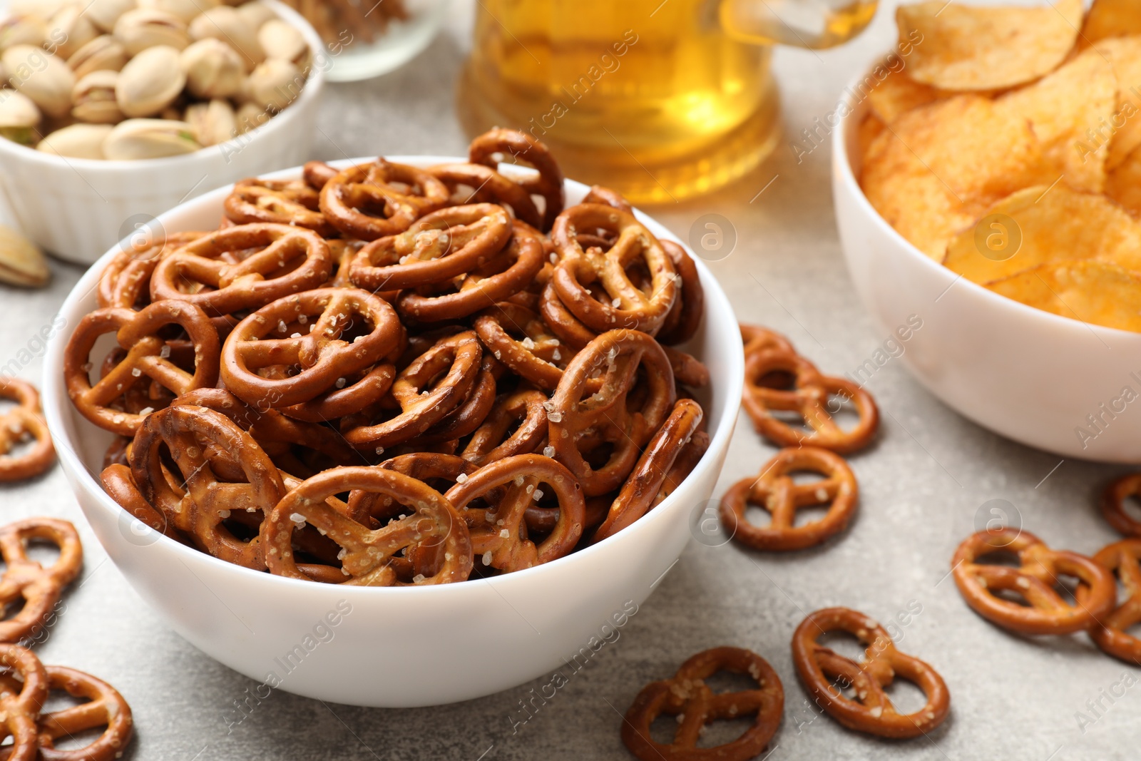 Photo of Delicious pretzel crackers, beer and other snacks on light table, closeup