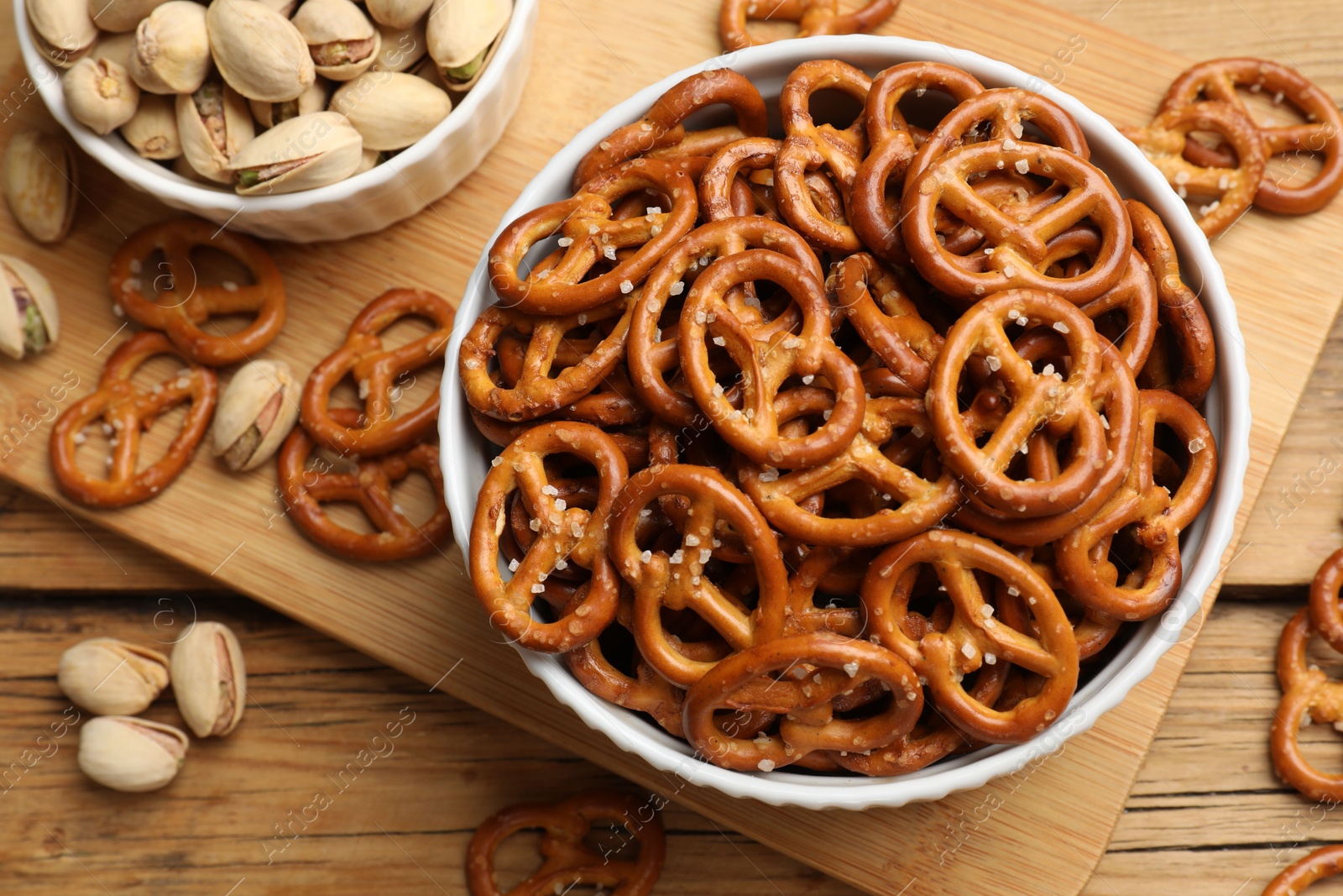 Photo of Delicious pretzel crackers and pistachios on wooden table, flat lay