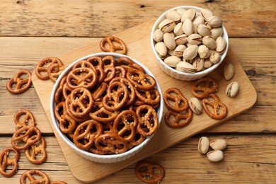 Photo of Delicious pretzel crackers and pistachios on wooden table, flat lay