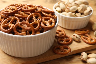 Photo of Delicious pretzel crackers and pistachios on wooden table, closeup