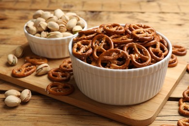 Photo of Delicious pretzel crackers and pistachios on wooden table, closeup