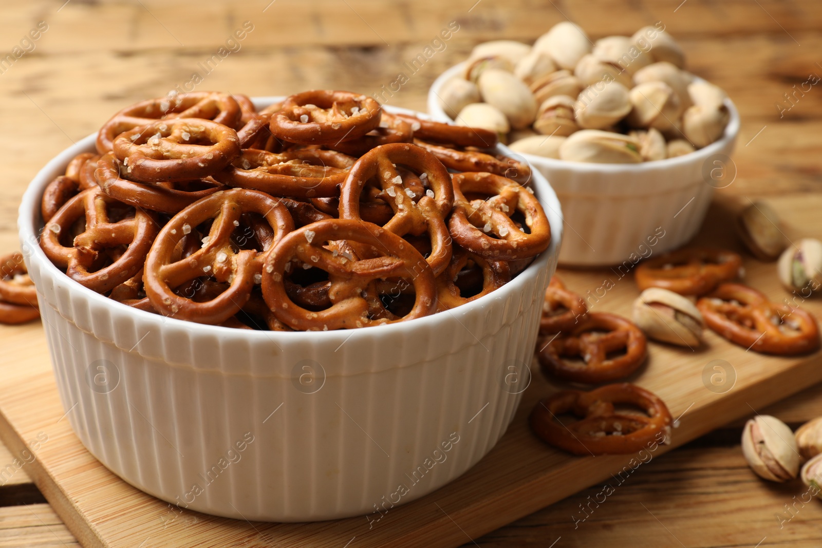 Photo of Delicious pretzel crackers and pistachios on wooden table, closeup