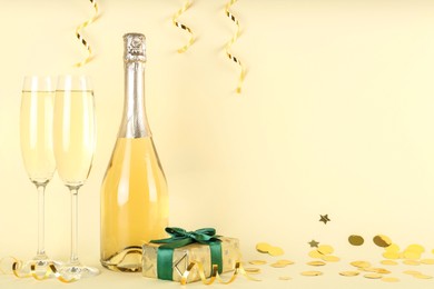 Photo of Shiny confetti, streamers, sparkling wine and gift box on beige background. Space for text