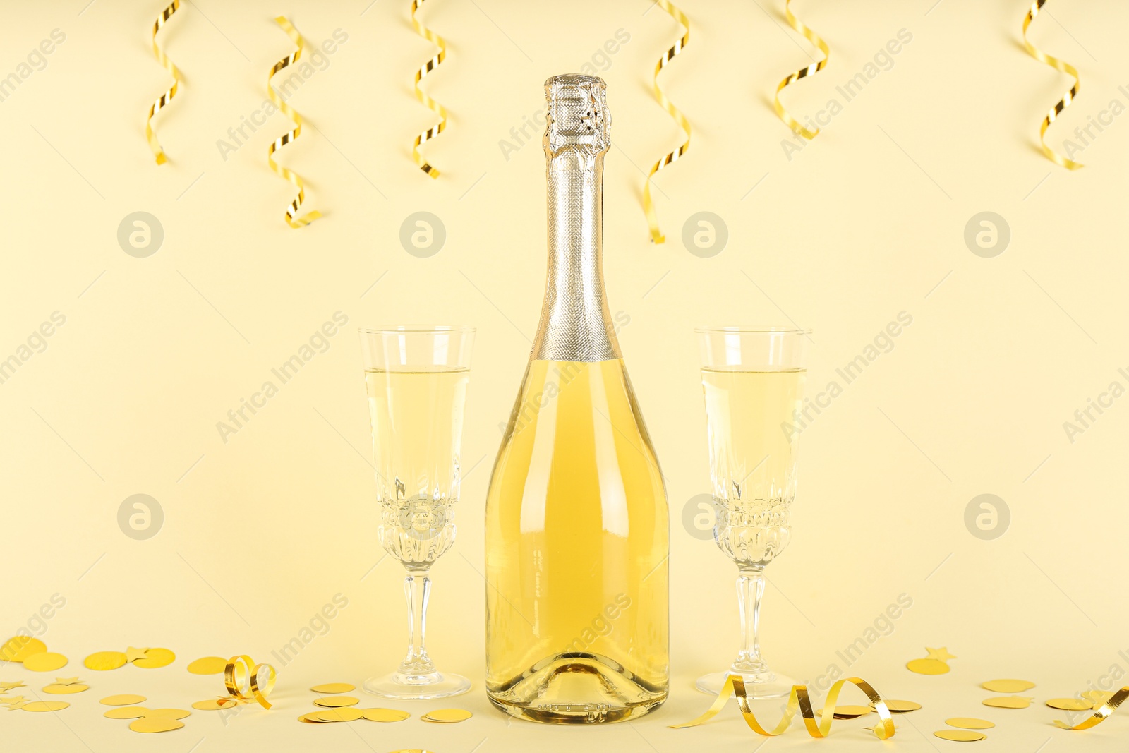 Photo of Shiny confetti, streamers and sparkling wine on beige background