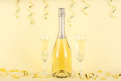 Photo of Shiny confetti, streamers and sparkling wine on beige background