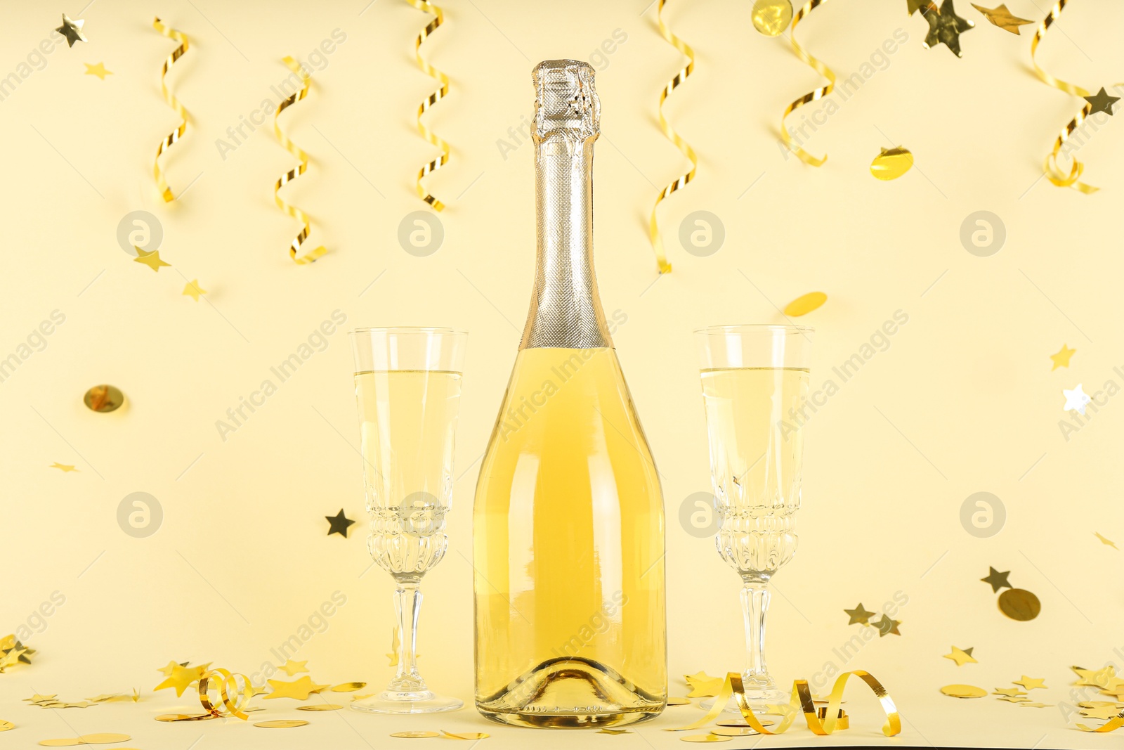 Photo of Shiny confetti, streamers and sparkling wine on beige background