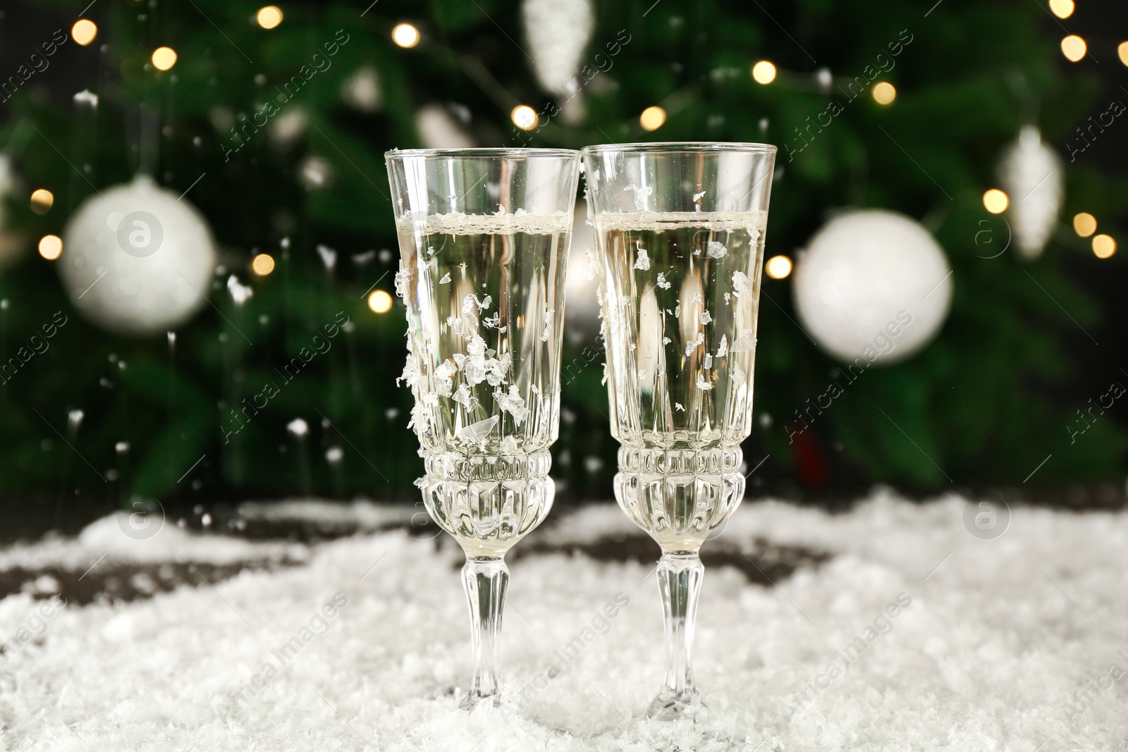 Photo of Sparkling wine in glasses and artificial snow on blurred background