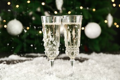 Photo of Sparkling wine in glasses and artificial snow on blurred background