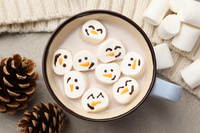 Photo of Marshmallows with snowmen faces in cup of hot drink on light table, top view