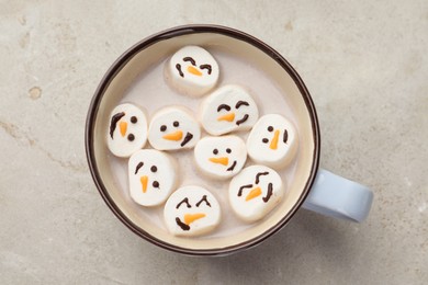 Photo of Marshmallows with snowmen faces in cup of hot drink on light table, top view