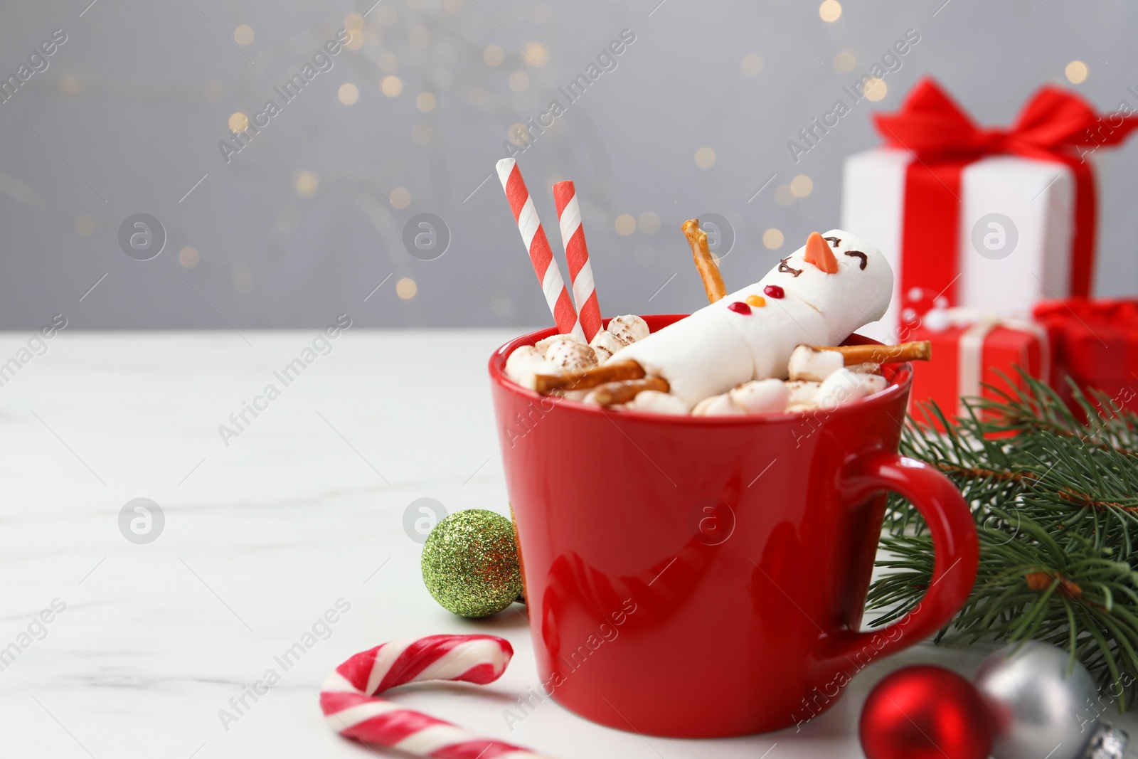 Photo of Funny snowman made with marshmallows in cup of hot drink and Christmas decor on white table. Space for text