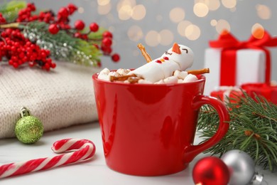 Photo of Funny snowman made with marshmallows in cup of hot drink and Christmas decor on white table