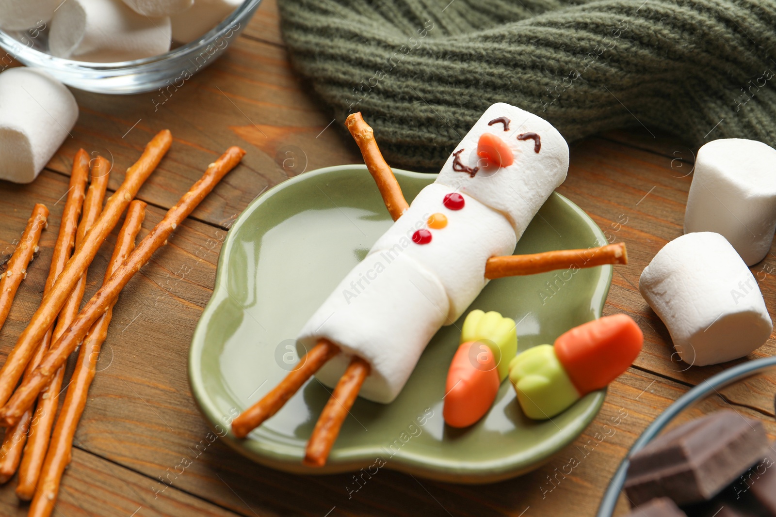 Photo of Funny snowman made with marshmallows, candies, chocolate and salty sticks on wooden table, closeup