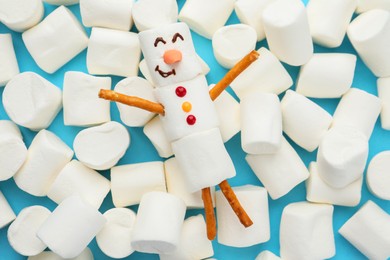 Photo of Funny snowman made of marshmallows and sweets on light blue background, top view