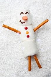 Photo of Funny snowman made of marshmallows on artificial snow, top view