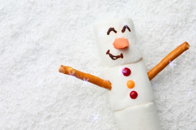 Photo of Funny snowman made of marshmallows on artificial snow, top view