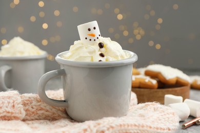 Photo of Funny snowman made with marshmallow and whipped cream in cup of hot drink served on background against Christmas lights, closeup